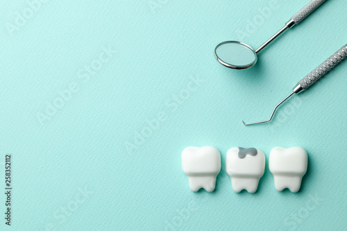 Healthy white teeth and tooth with caries on green mint background  and dentist tools mirror, hook. Copy space for text. photo