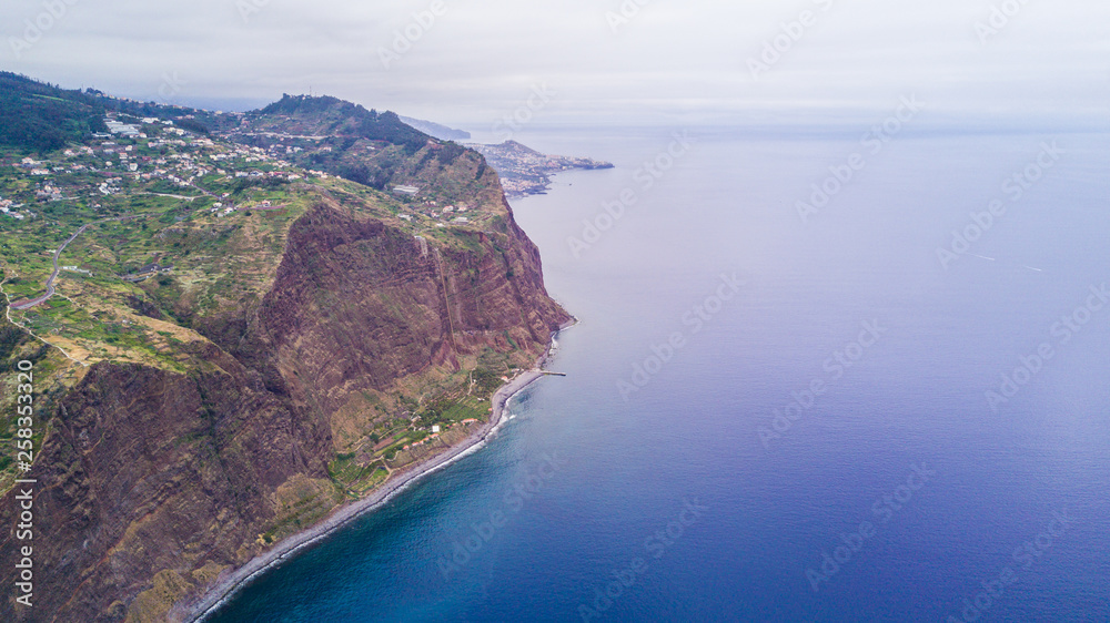 Aerial panoramic cityscape view of the cities in madeira with houses in front and covered mountains and white clouds