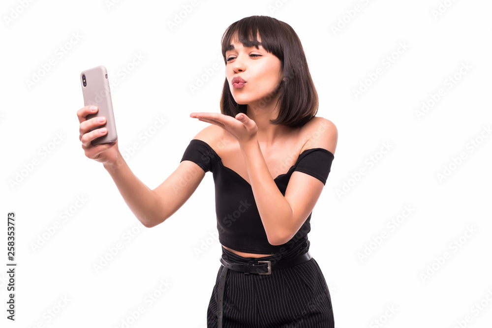 Portrait of a lovely young woman dressed taking a selfie and blowing air kiss isolated over white background Portrait of a lovely young woman dressed taking a selfie and blowing air kiss isolated over white background