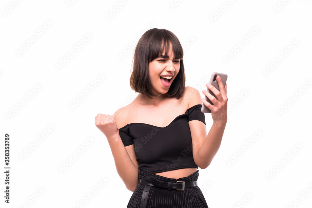Portrait of a happy excited girl holding mobile phone and celebrating win isolated over grey background Portrait of a happy excited girl holding mobile phone and celebrating win isolated over grey background