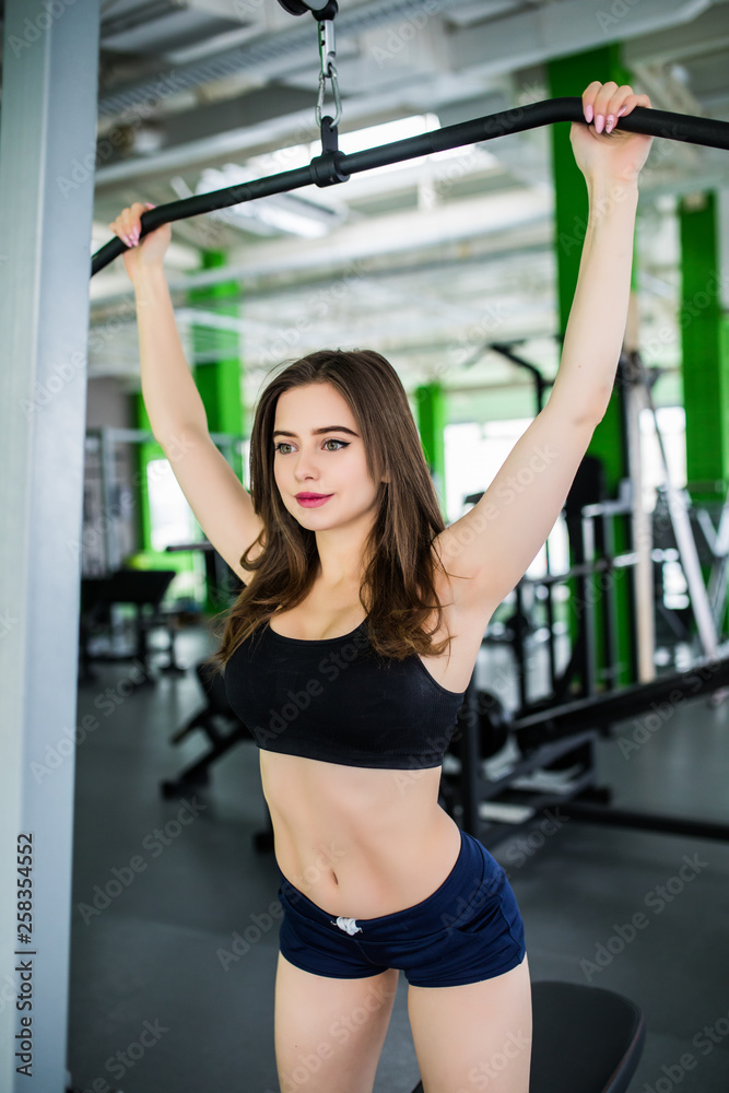 Attractive woman exercising at gym, biceps workout on a machine.