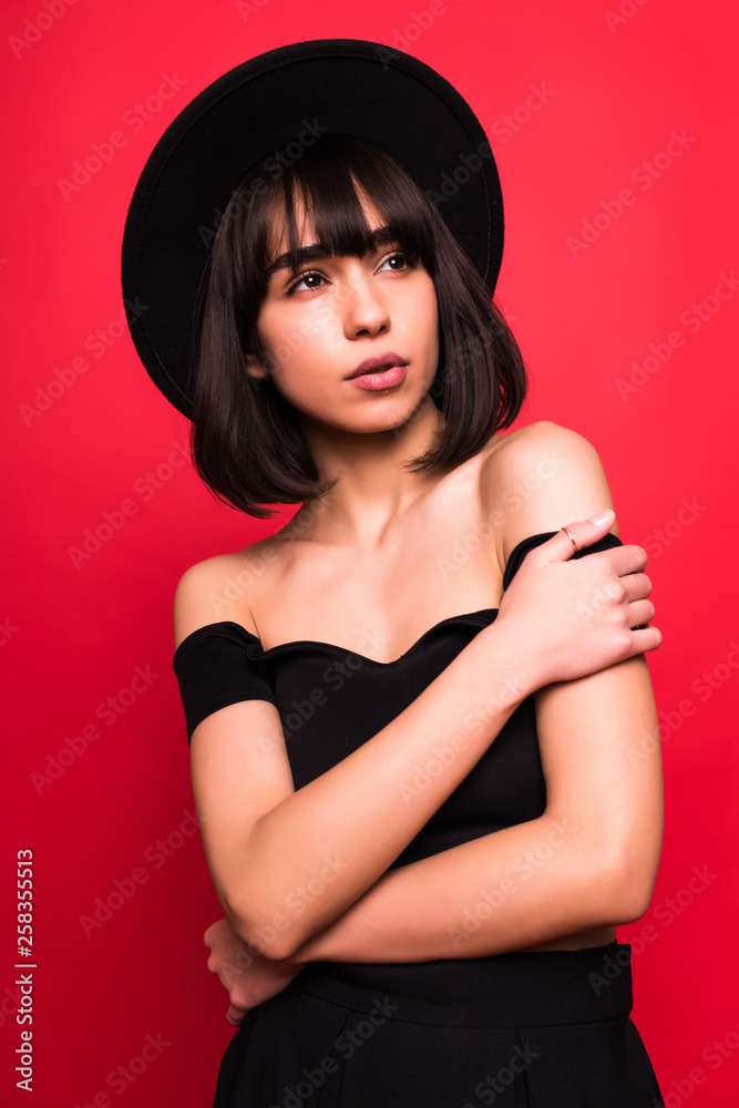 Young brunette woman in fluppy black hat and black clothes on red background Young brunette woman in fluppy black hat and black clothes on red background