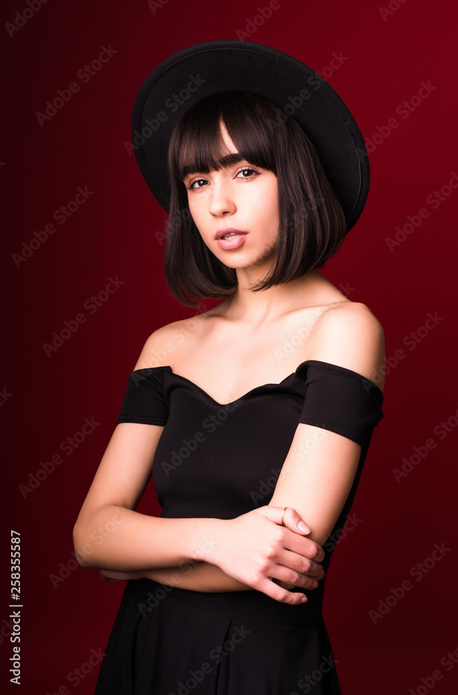 Young pretty woman in black hat isolated on red background Young pretty woman in black hat isolated on red background