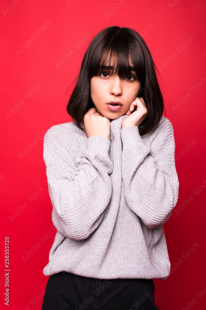Attractive woman in sweater standing isolated on red background Attractive woman in sweater standing isolated on red background