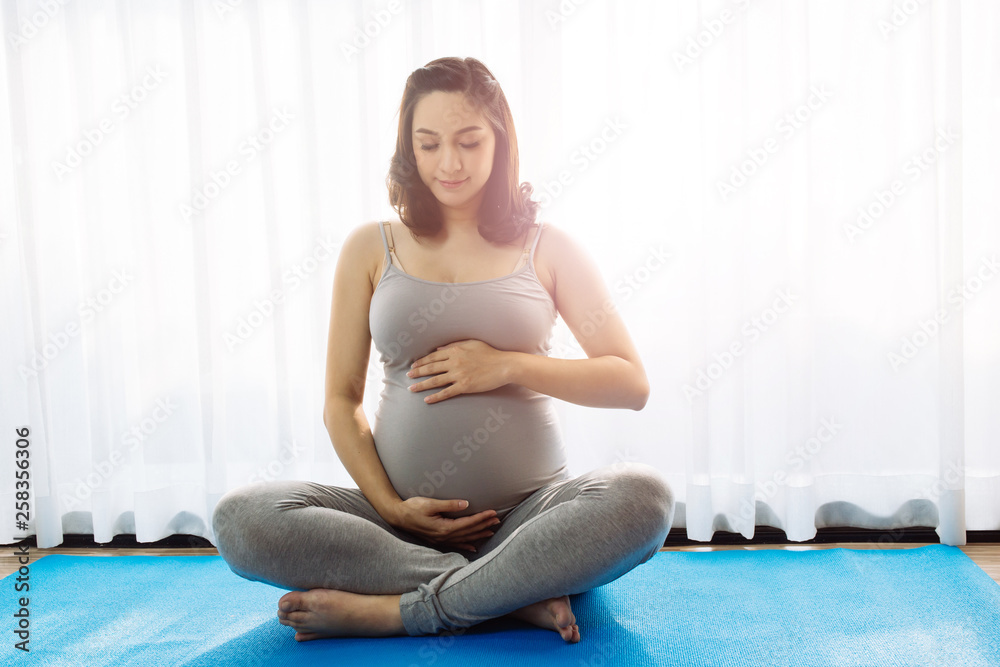 Young attractive pregnant woman holding and touching her pregnant tummy inside home