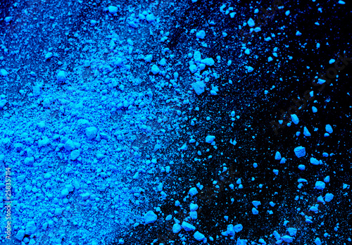 Pile of blue colored pigment powder. Blue powder particles splatter on black blackground.