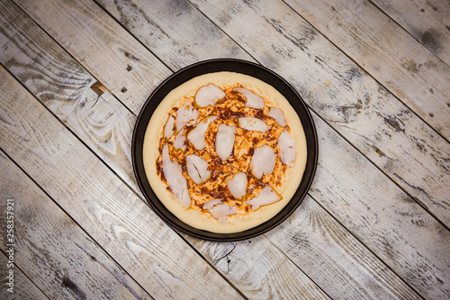 Round pizza dough is in the pan. The process of cooking pizza, stacking ingredients on the dough.