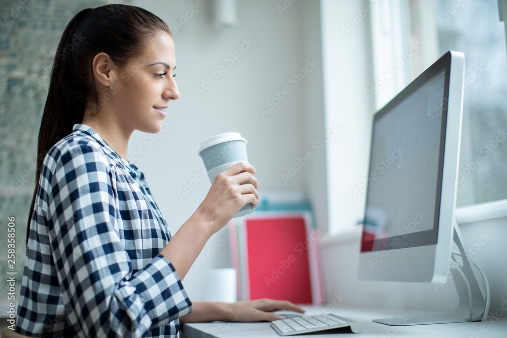 Woman Working At Computer Drinking From Reusable Takeaway Cup Woman Working At Computer Drinking From Reusable Takeaway Cup