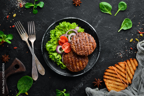 fried cutlet for burger with vegetables. In a black plate on a wooden background Top view. Free space for your text. Flat lay photo