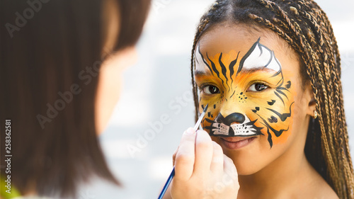 Adorable african-american girl getting tiger face painting photo