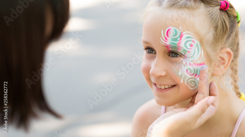 Cute little girl getting her face painted in park photo