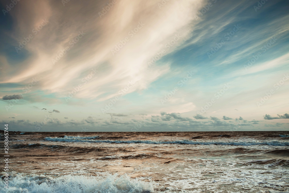 Obraz premium Beautiful sunset over wavy Baltic sea. Soft blue color and white yellow clouds on the sky.