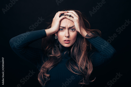 Upset offended beautiful woman holding her hands on head isolated on black background