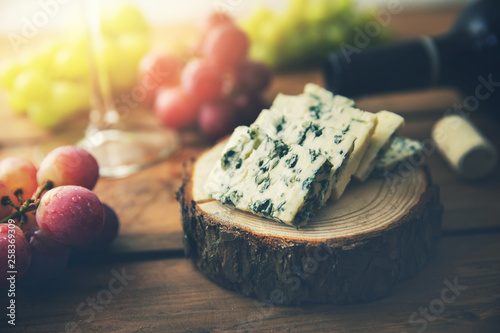 dor blue cheese on wood log slice with grapes and wine bottle photo