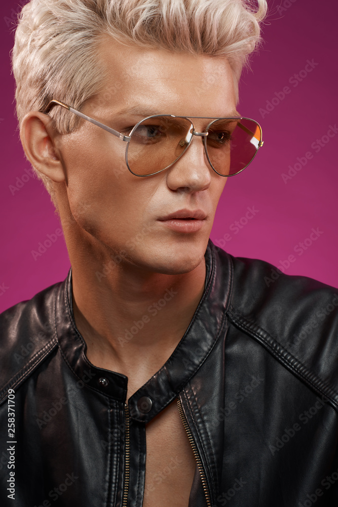 Blond haired young man in yellow glasses close up portrait on pink background Blond haired young man in yellow glasses close up portrait on pink background
