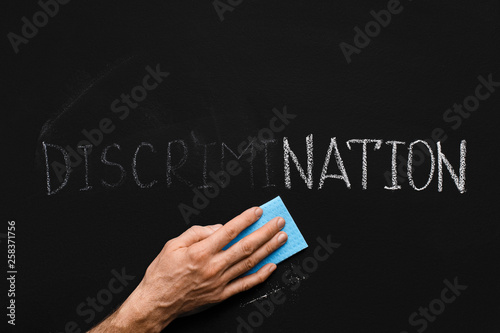 Foto Male hand cleaning word DISCRIMINATION on chalkboard