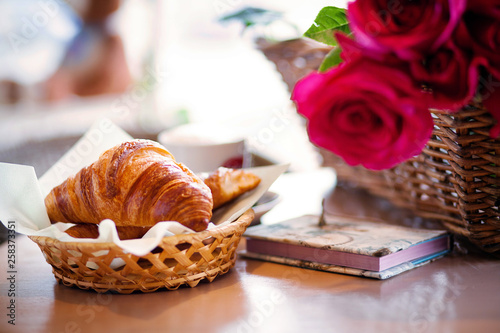 croissants in a wicker plate next to flowers and a notebook