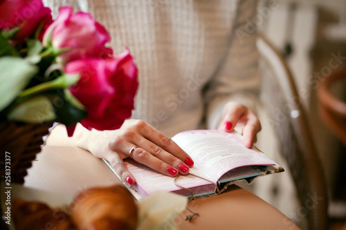 girl on the background of flowers reading a book close up the book and hands