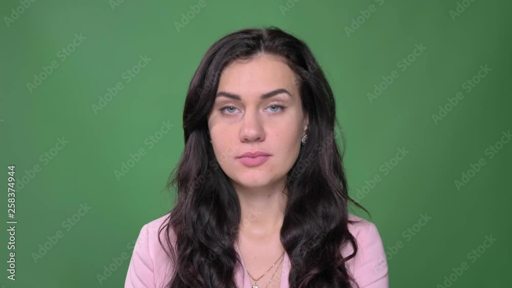 Young brunette businesswoman in pink jacket watches seriously and modestly into camera on green background. Young brunette businesswoman in pink jacket watches seriously and modestly into camera on green background.