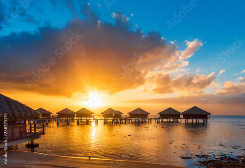 Water Bungalows with a idyllic sunset, beautiful sky and clouds in the lagoon Huahine, French Polynesia. Copy space for text.