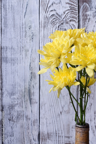 Bouquet of yellow chrysanthemum flowers in a vintage bottle against the white wooden background