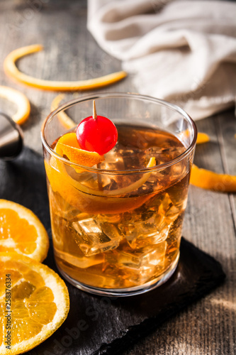 Old fashioned cocktail with orange and cherry on wooden table