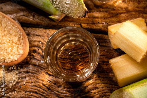 two shot glasses of Brazilian gold  cachaca with sugar and sugarcane isolated on rustic wooden background