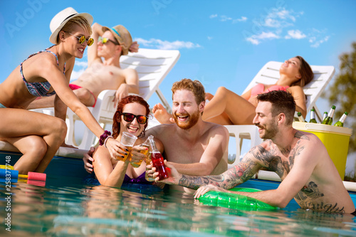 Принти на полотні Cheerful men and women toasting with drink in swimming pool