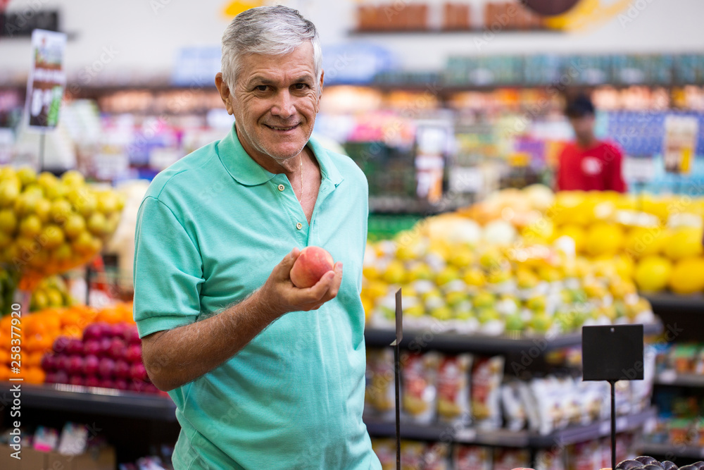 Handsome man posing, looking and holding fruit in hand. Bearded customer smiling. Section with fresh citruses on background