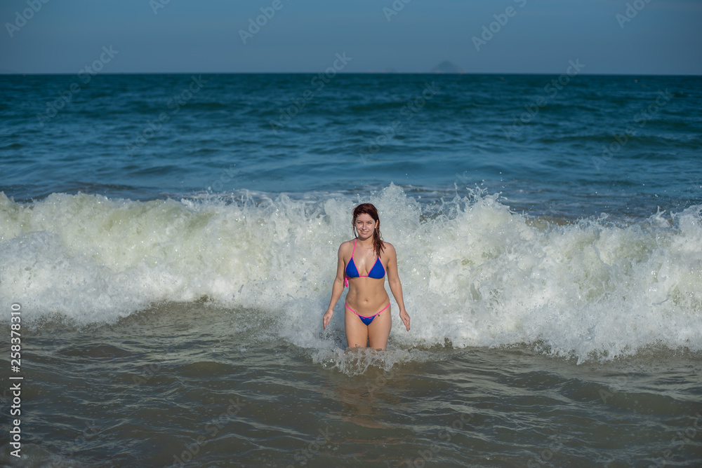 beautiful young woman in a seductive bikini comes out of the sea with high waves. Big waves in the ocean