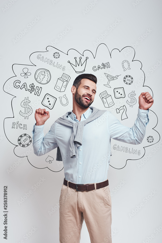 I won! Happy young man is celebrating his success with raised hands while standing against grey background with different doodle illustrations on it. Gambling concept. I won! Happy young man is celebrating his success with raised hands while standing against grey background with different doodle illustrations on it. Gambling concept.