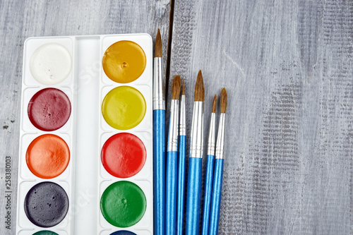 A palette of watercolor paints and brushes of different sizes, lying on a gray wooden background photo