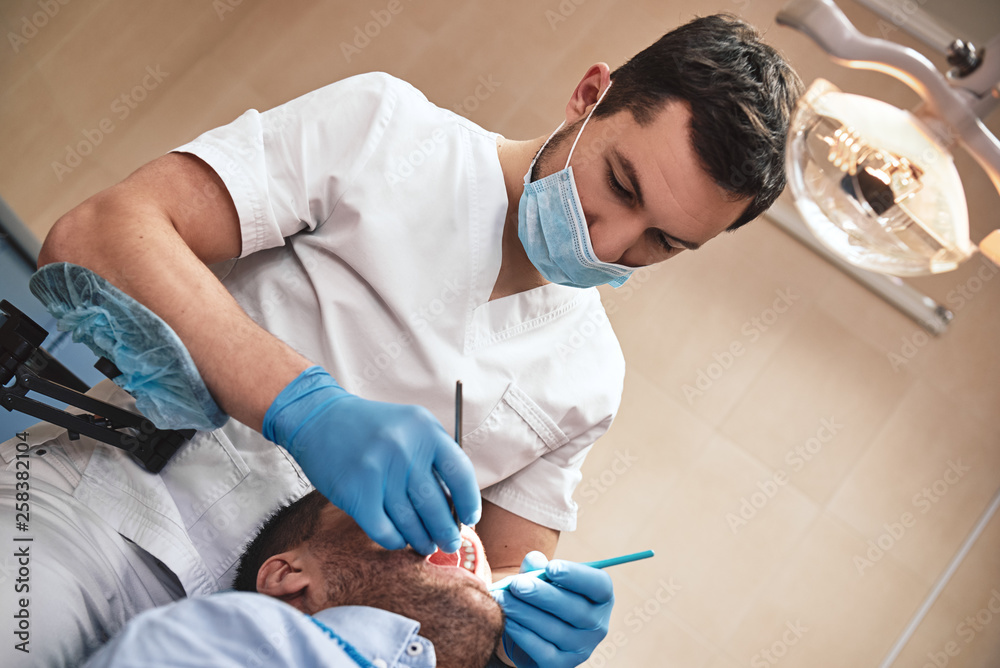 Nothing but the tooth. Dentist in latex gloves examining male patient, lying in dental chair with opened mouth Nothing but the tooth. Dentist in latex gloves examining male patient, lying in dental chair with opened mouth
