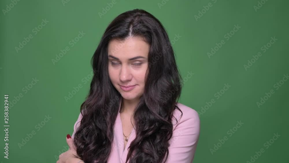 Young brunette businesswoman in pink jacket watching with flirting and mysterious smile into camera on green background. Young brunette businesswoman in pink jacket watching with flirting and mysterious smile into camera on green background.
