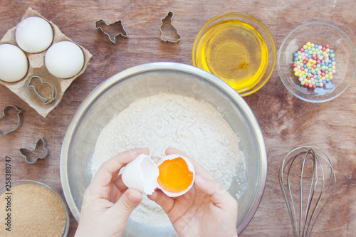 Hands of a child in the process of preparing Easter cookies dessert, biscuit with kitchen tools and products on a wooden table. Close up concept of family leasure. Top view flatlay