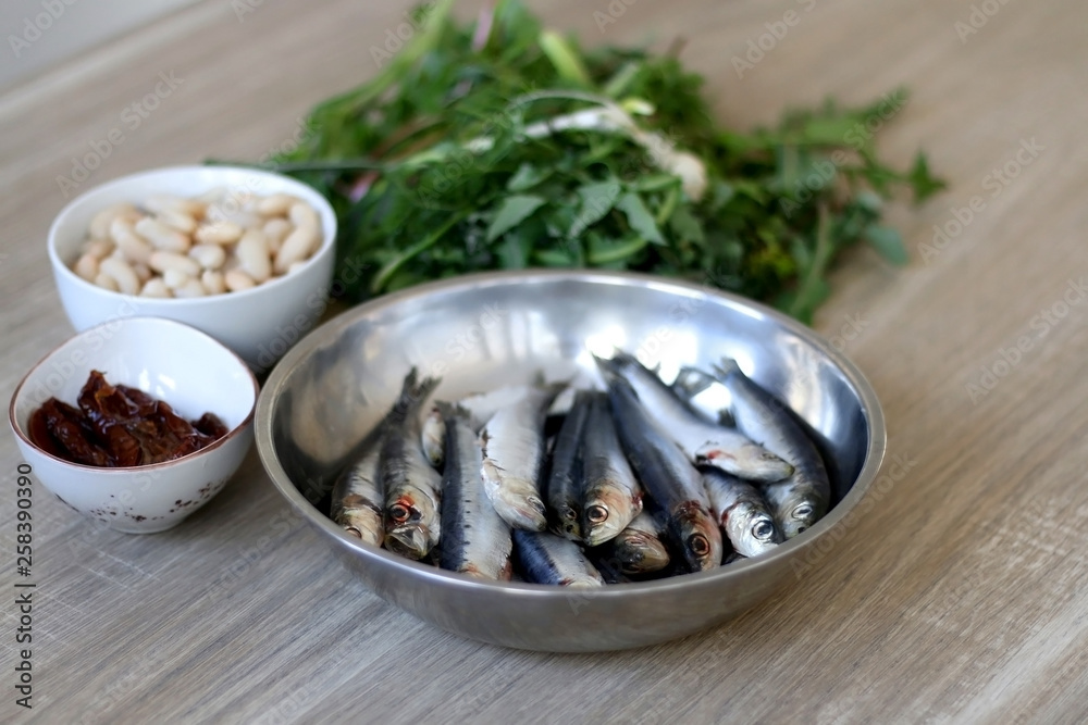Fresh sardines, white beans, dried tomatoes and chicory on a wooden table. Ingredients for a meal. Selective focus. Fresh sardines, white beans, dried tomatoes and chicory on a wooden table. Ingredients for a meal. Selective focus.