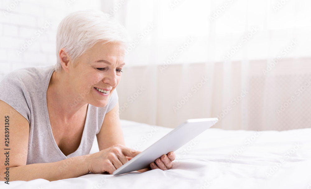 Happy senior woman lying in bed and using digital tablet Happy senior woman lying in bed and using digital tablet