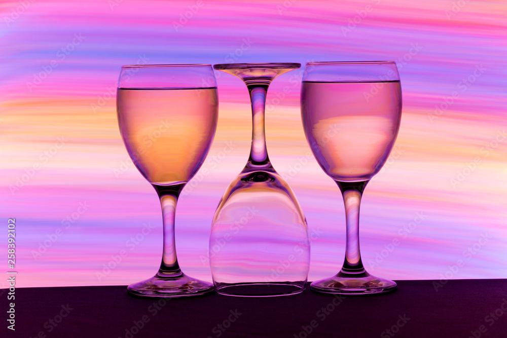 Three wine glasses in a row with colorful light painting behind Three wine glasses in a row with colorful light painting behind