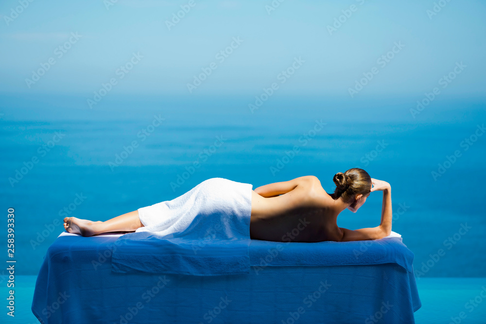 Woman on massage table facing sea - obrazy, fototapety, plakaty 