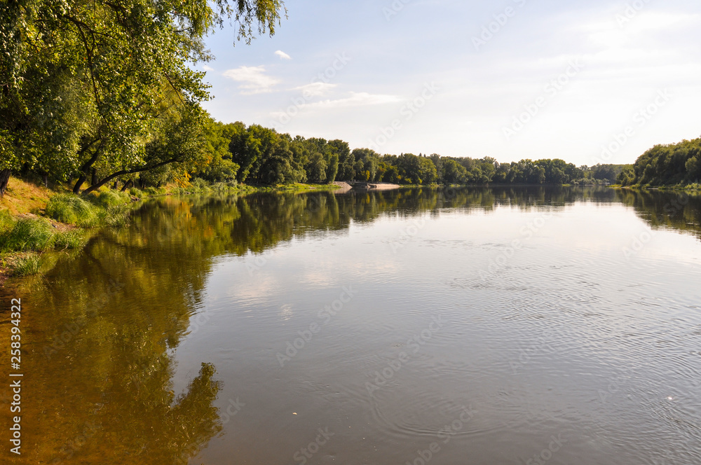 Wide yellow river is slow flowing. Early autumn. Sunny weather and brightgreen trees on the banks fron the both sides Wide yellow river is slow flowing. Early autumn. Sunny weather and brightgreen trees on the banks fron the both sides