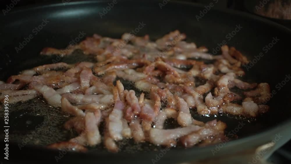 Slowmo Close Up, Bacon pieces sizzling in grease in black frying pan