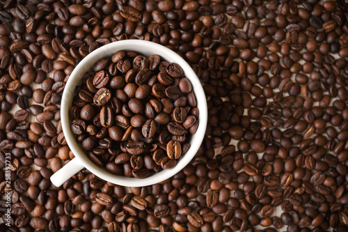 white cup with roasted coffee beans stands on the background of a large number of coffee beans