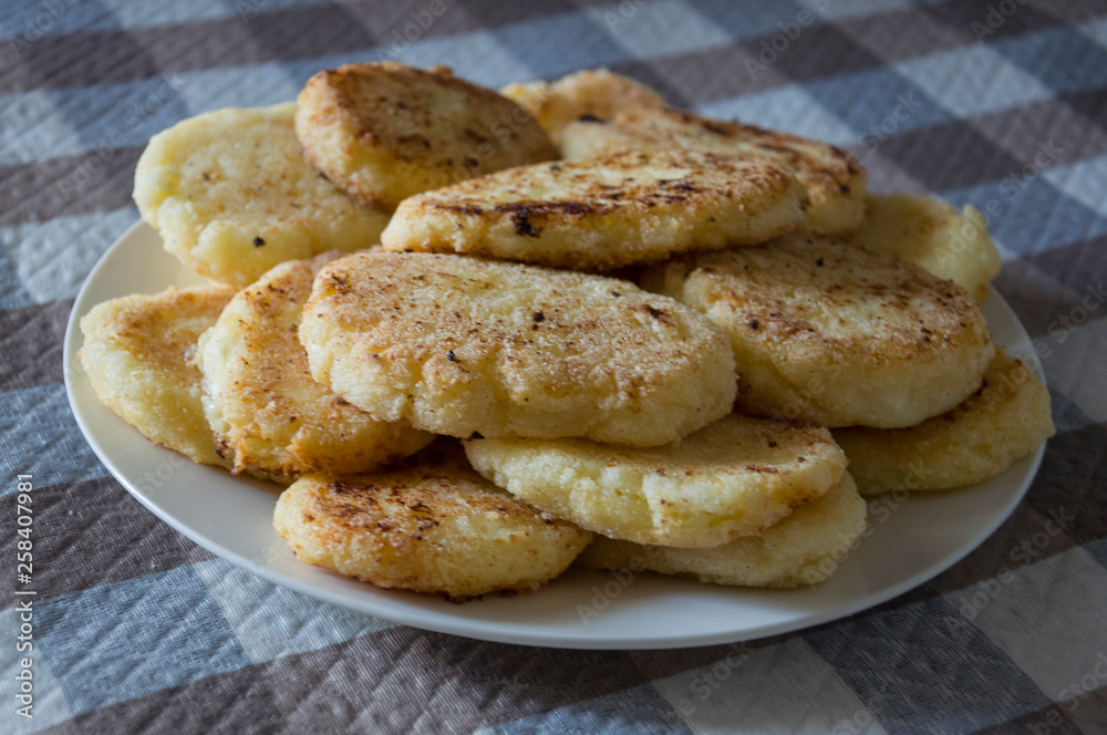Hot tasty baked cheese pancakes in the plate standing on the checkered tablecloth. Breakfast Hot tasty baked cheese pancakes in the plate standing on the checkered tablecloth. Breakfast