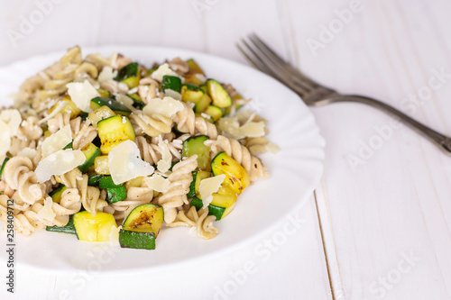 Recipe step by step fusilli pasta with zucchini closeup on white porcelain plate with a fork on white wood photo