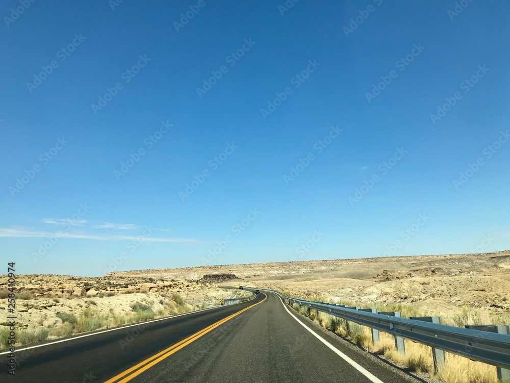 A photo showing an empty asphalt road in a desert climate, made sunny on a clear day. A photo showing an empty asphalt road in a desert climate, made sunny on a clear day.