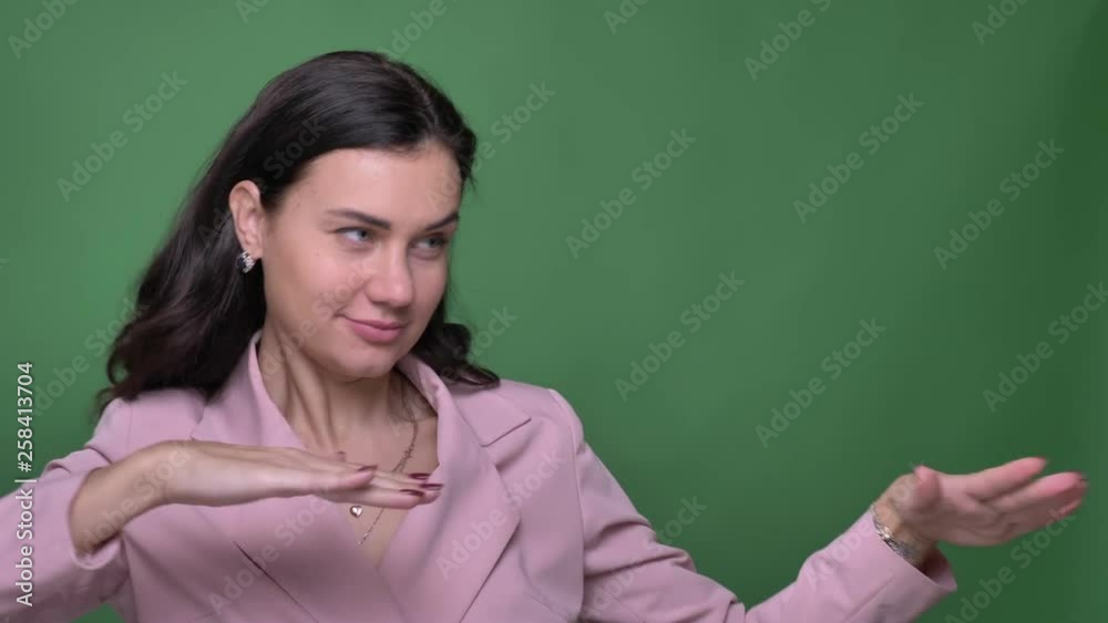 Portrait of young brunette female vloger in pink jacket dancing strangely and winking at camera on green background. Portrait of young brunette female vloger in pink jacket dancing strangely and winking at camera on green background.