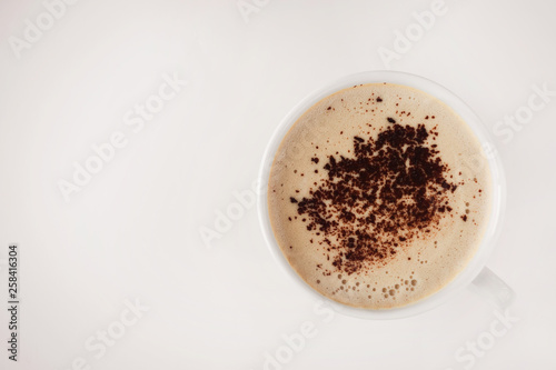 white cup with cappuccino and frothy and grated chocolate on a beige background and free space for the inscription on the left