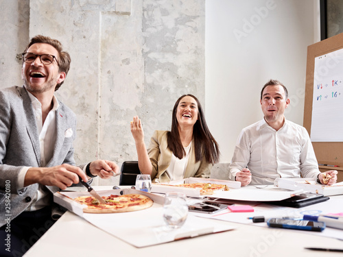 Laughing colleagues having lunch break with pizza in conference room