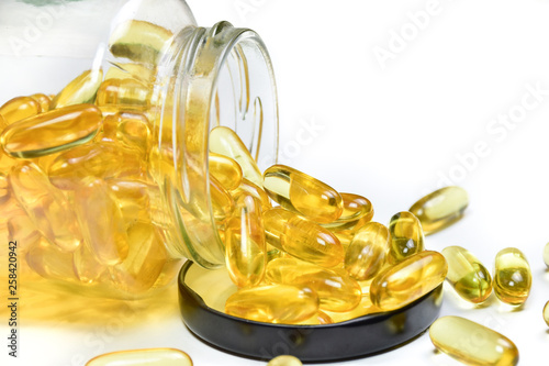Close up of fish oil capsules in a glass bottle on white background. Omega 3. Vitamin E. Supplementary food background.
