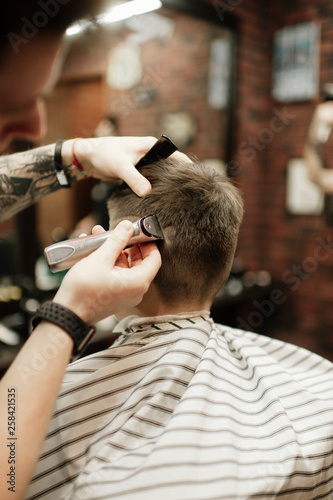 man being trimmed with electric clipper machine in barbershop.Male beauty treatment concept. Young guy getting new haircut in barber salon